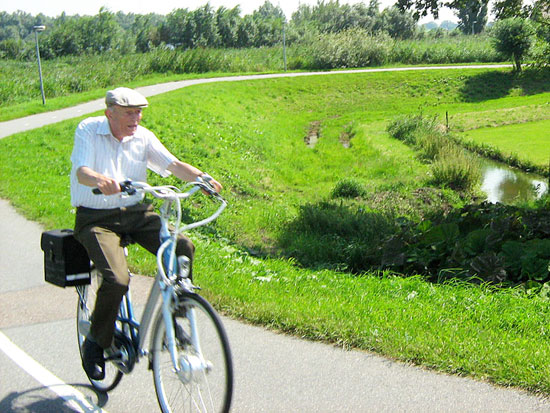 An elderly man uses a practical bicycle for transport in the Dutch countryside.