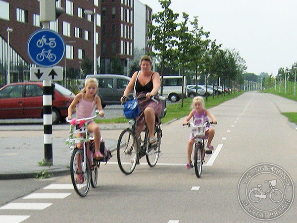 A mother and her two young daughters ride their bikes on a wide cycle path