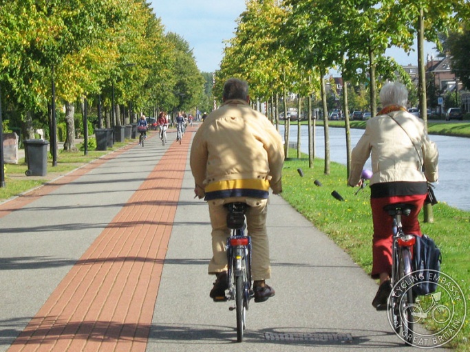 An older couple riding on a tree-lined bicycle street alongside a canal